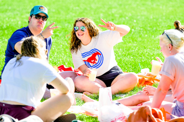 People sit on the lawn at SMU having a picnic, holding up SMU Peruna pony ears