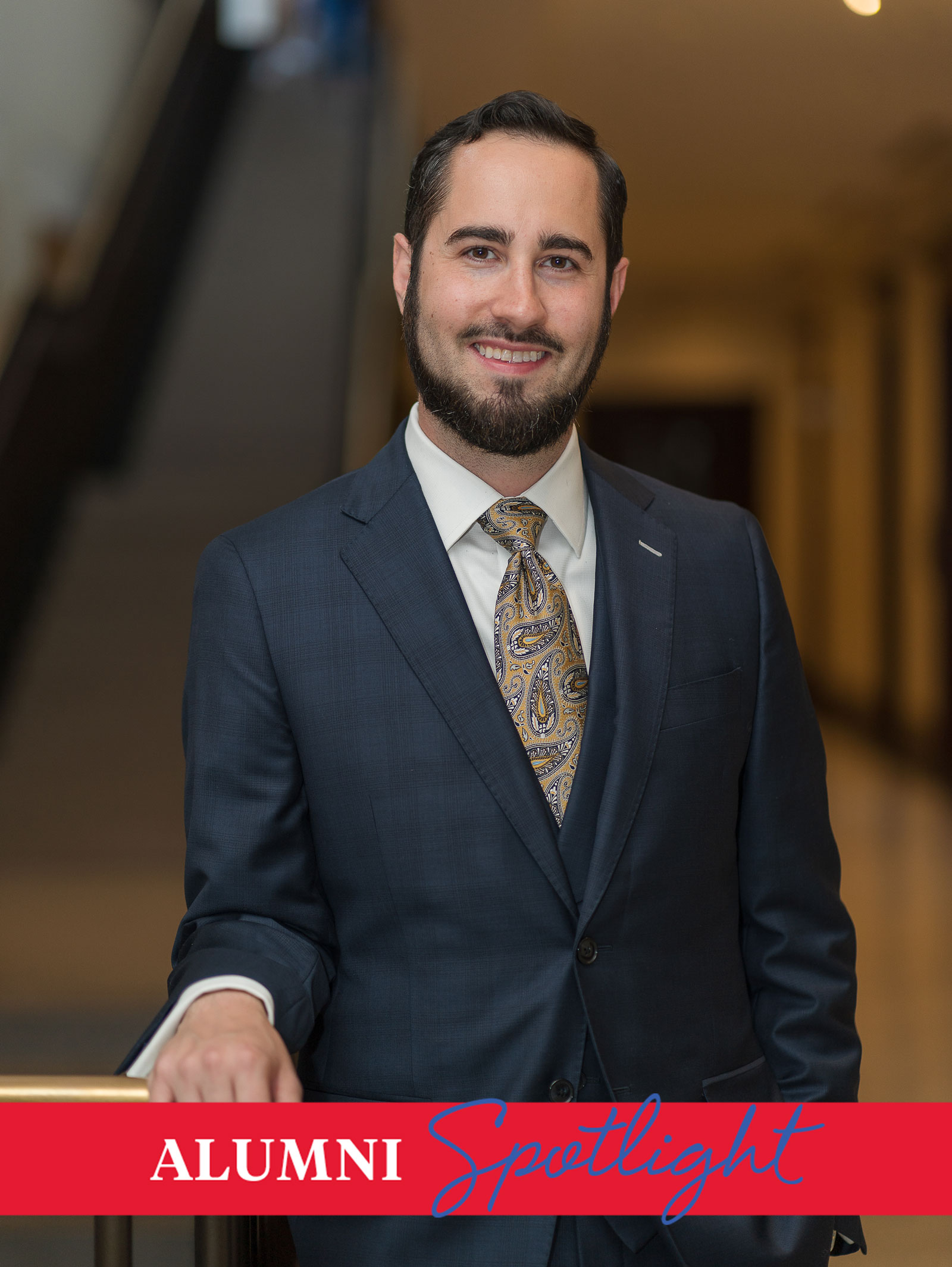 Music alum Derek W. Hawkes poses in front of a hallway wearing a suit and tie